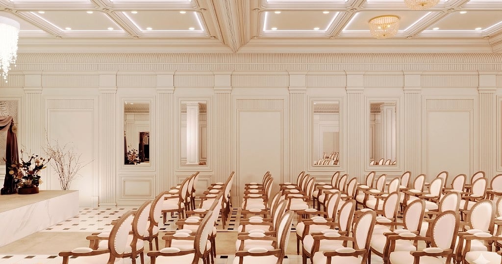 Rows of oval-back wooden chairs facing a marble ceremony stage with florals, framed by fluted walls, a coffered ceiling and a checkerboard marble floor