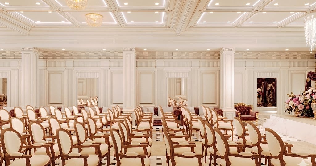 A ceremony setup in the banquet hall, oval-back chairs before a draped stage with a tufted throne and florals, against ivory panelled walls