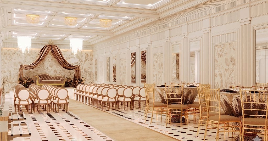 The draped ceremonial stage and seating against a soft botanical feature wall, with gold banquet tables to one side under chandeliers