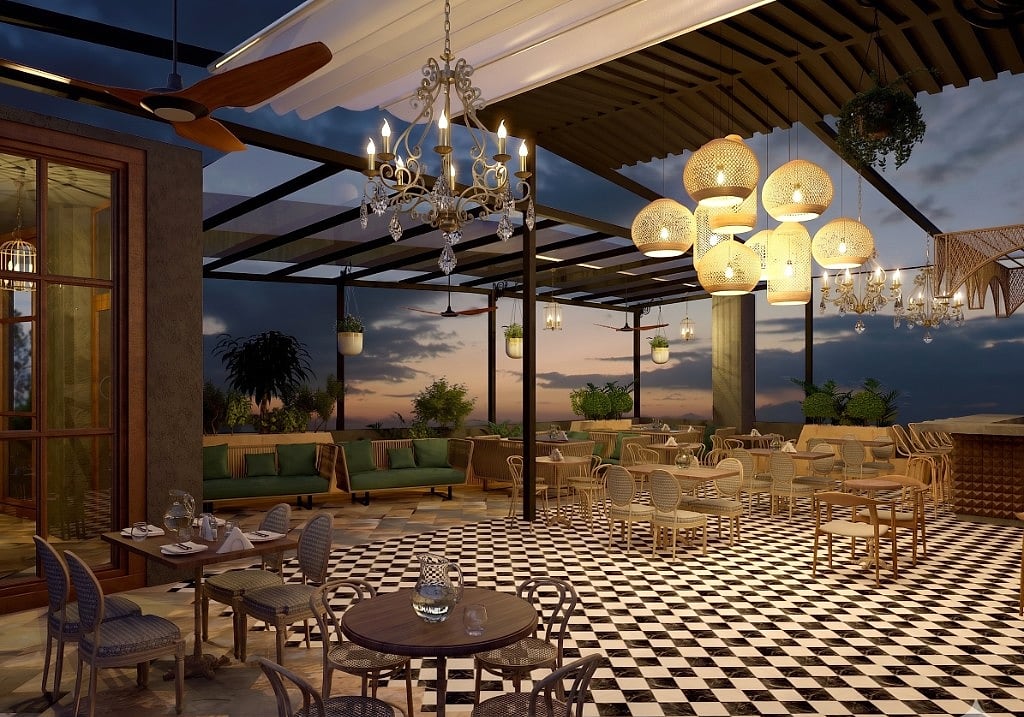 The open side of the terrace cafe at sunset, a white awning and pergola, ornate chandelier and woven rattan pendant cluster over checkerboard floors, green banquettes and layered greenery