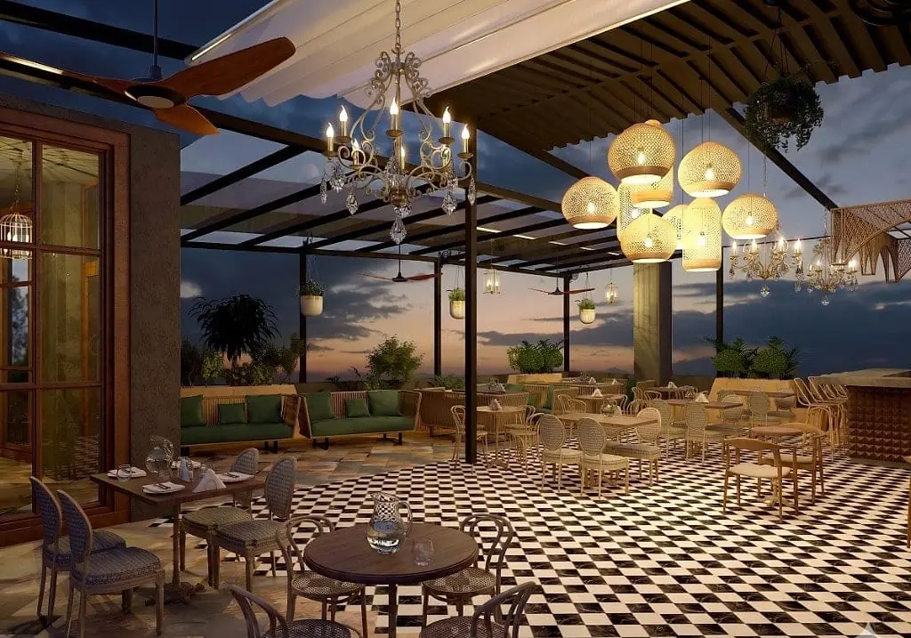 The open side of the terrace cafe at sunset, a white awning and pergola, ornate chandelier and woven rattan pendant cluster over checkerboard floors, green banquettes and layered greenery