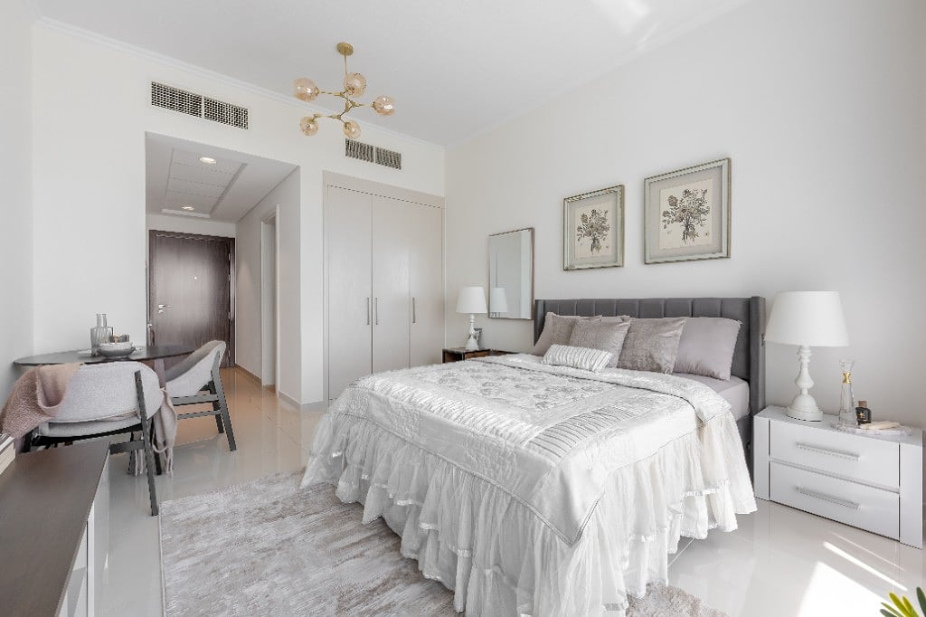 The Damac Hills apartment furnished by ZuriSpace, a bright open room with a grey upholstered bed, gold orb chandelier, silver-framed botanical prints and a compact dressing nook