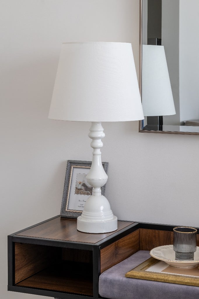Close detail of a white turned-wood lamp and a framed photograph on a walnut-and-black mid-century console below a bevelled mirror