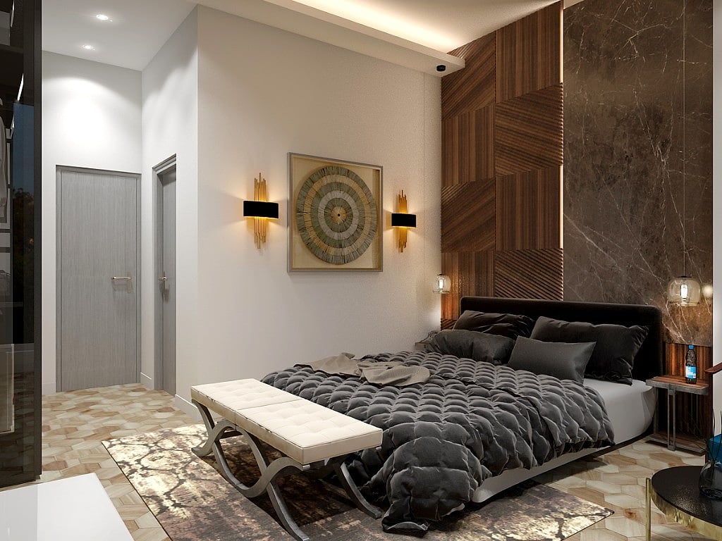 A guest room with an upholstered headboard against a textured concrete-panel feature wall, herringbone timber floor, a grey bench at the foot of the bed and a seating corner by the window
