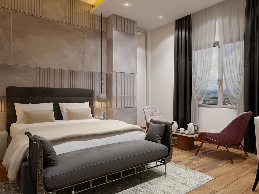A guest room with a herringbone wood and brown marble feature wall, a dark upholstered bed, a white bench, brass wall sconces and a circular mandala artwork
