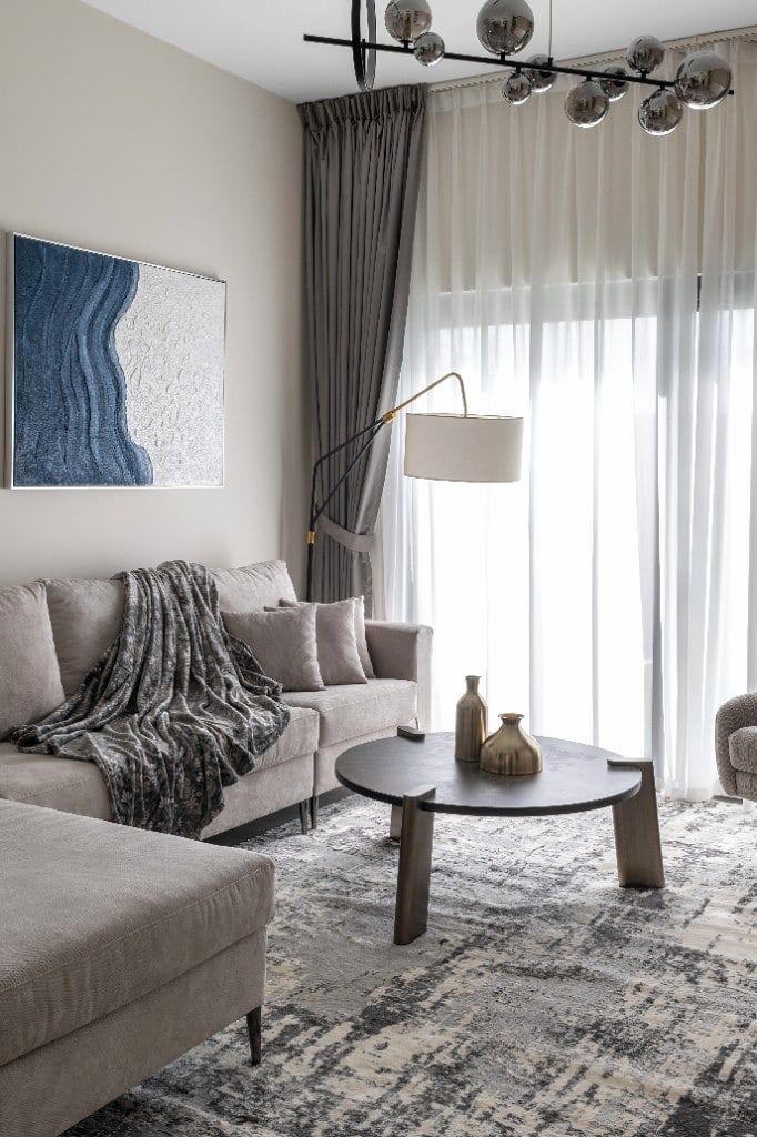 Living room from the second sofa, cobalt wave canvas above a grey velvet two-seater with a brass arc floor lamp behind