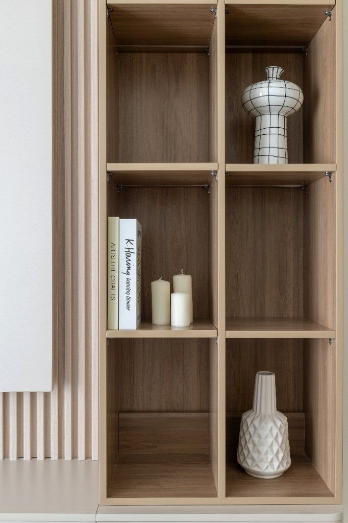 TV-unit close-up, the open oak shelving on the media wall styled with a patterned ceramic urn, a textured white vase, candles and a stack of art books beside the vertical fluted-oak panelling