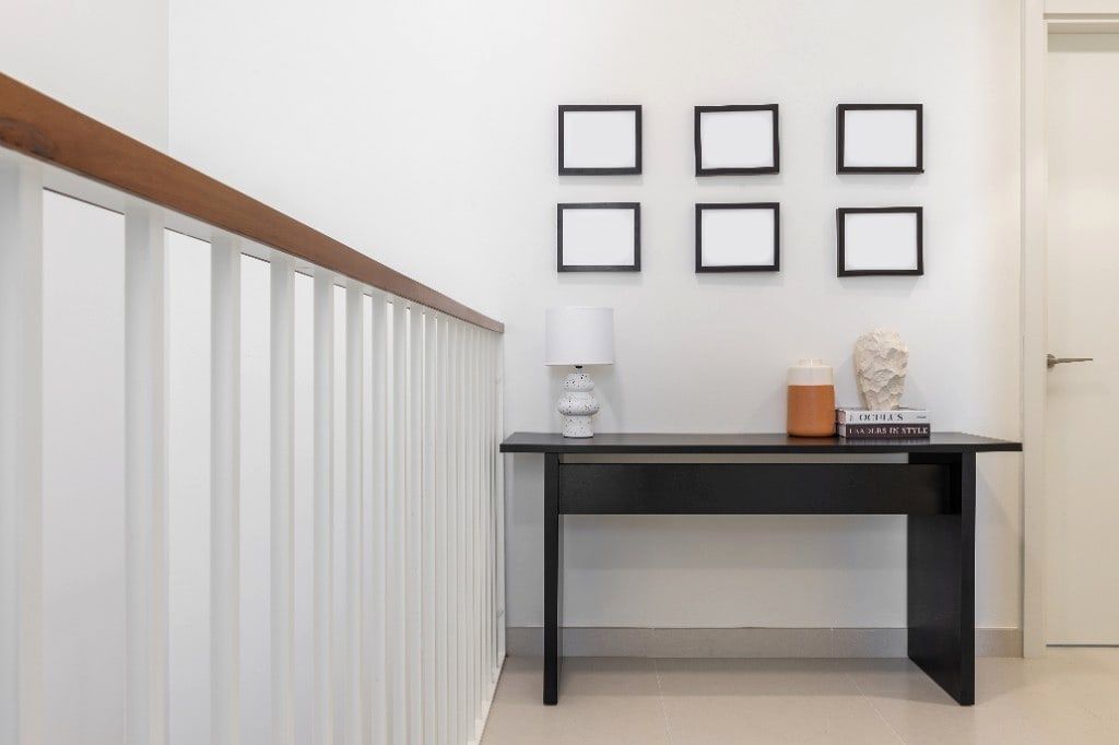 Upstairs landing styled with a slim black console, a six-frame gallery wall, a sculpted lamp and a plaster bust