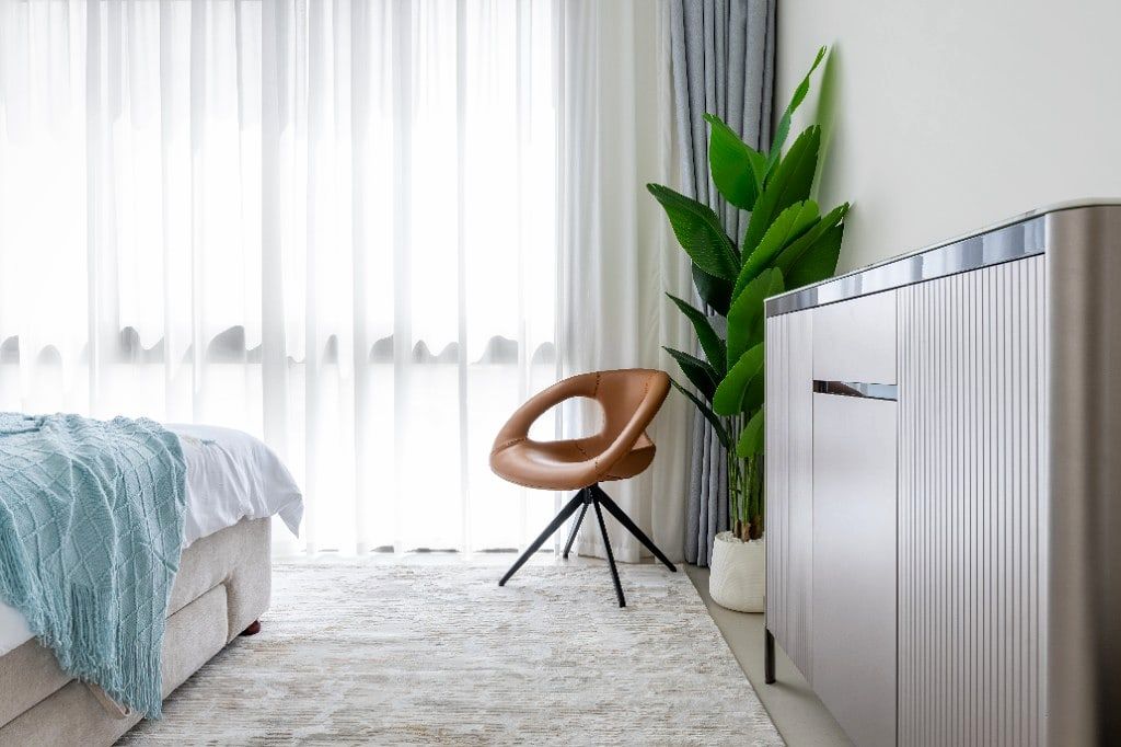 Master bedroom of the Pulse villa with sheer linen curtains, a brown leather saucer chair and a bird-of-paradise plant