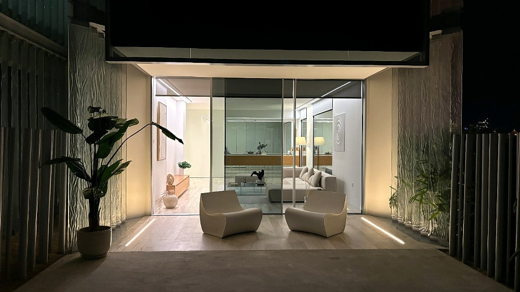 Palm Jumeirah apartment terrace pavilion at night, sculptural cream lounges flanking the glazed entry into the warmly lit living room