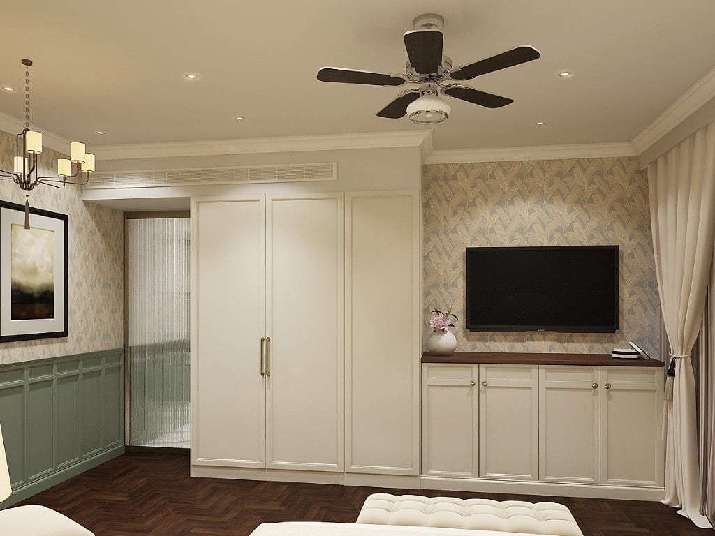 A suite bedroom with cream built-in wardrobes, a wall-mounted TV over a media-and-minibar cabinet on patterned wallpaper, sage wainscoting and herringbone parquet